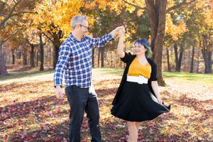A couple dances together in a park during autumn with golden leaves falling around them.