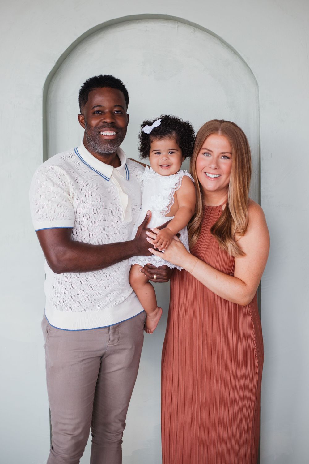 A family poses for a portrait in an arched doorway, wearing coordinated casual outfits.