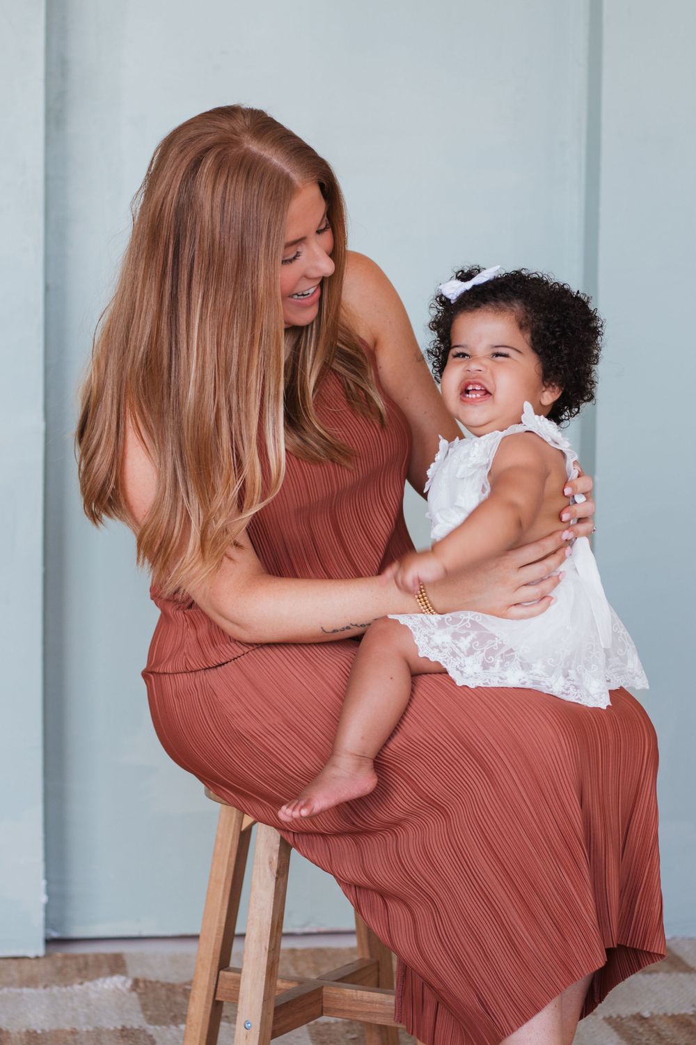 A sweet moment captured between parent and child sitting on wooden stool against light blue wall.