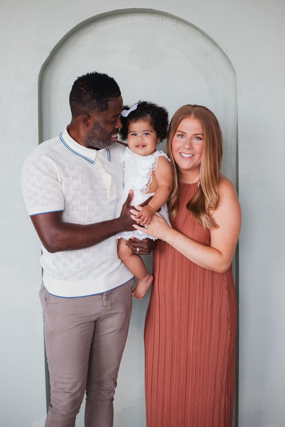 A family poses together under an arched doorway wearing coordinated white and terracotta outfits.