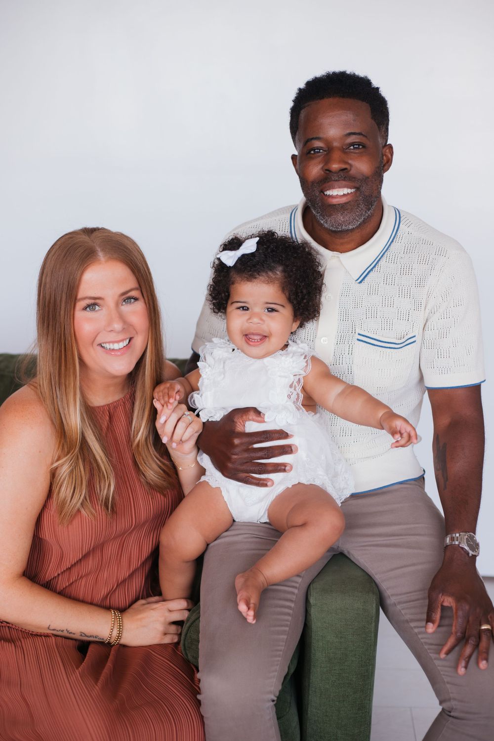 Family poses together on green couch for professional studio portrait in coordinated outfits.
