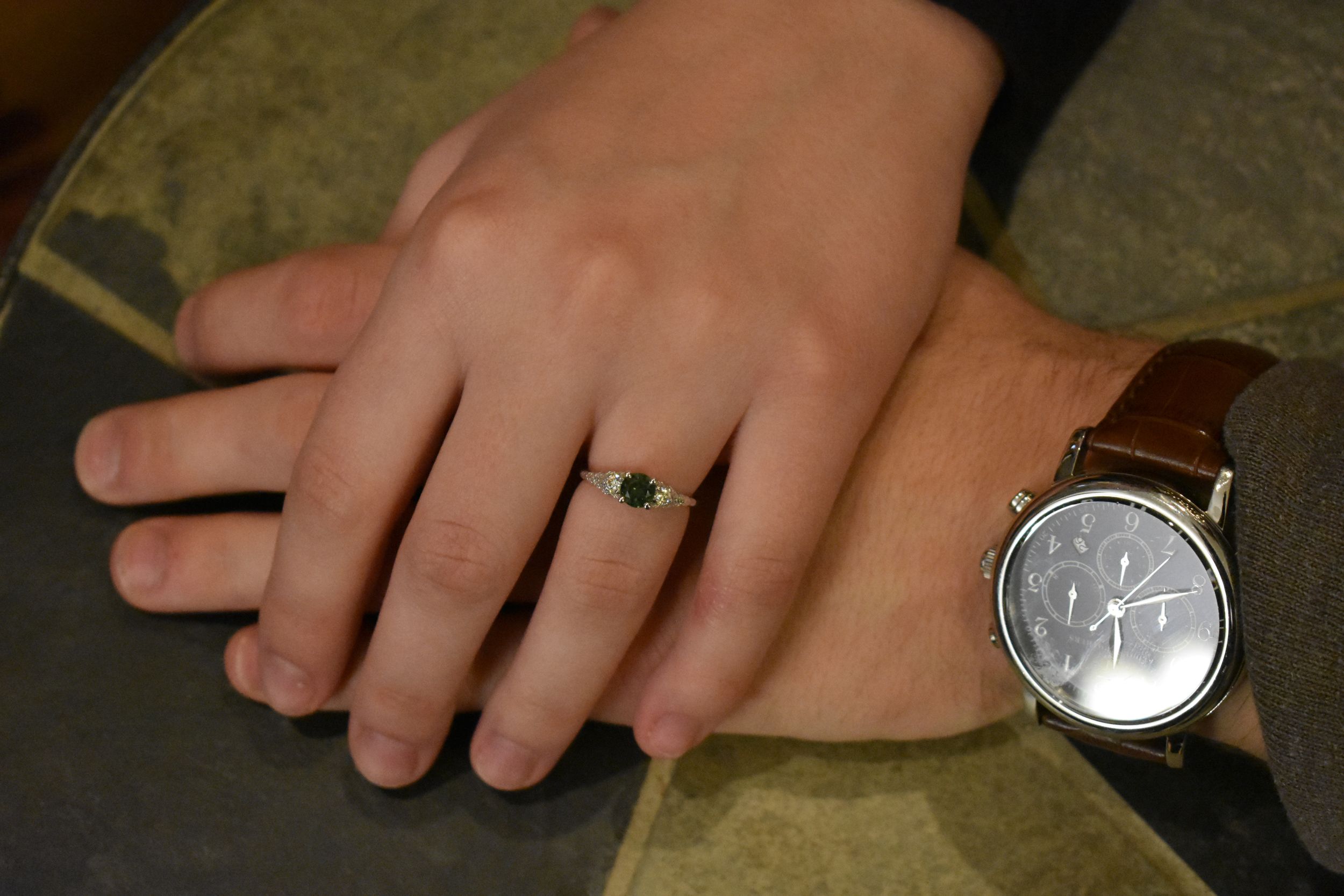 Close-up of hands showing off an engagement ring and leather watch.