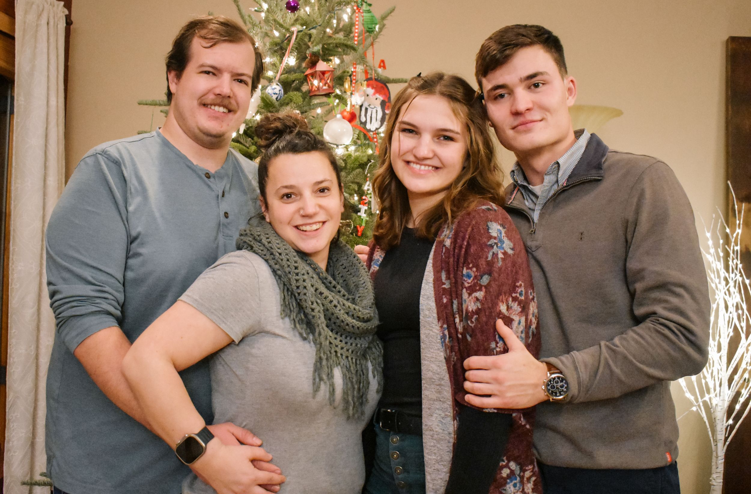 Group photo of four people posing together in front of a decorated Christmas tree.