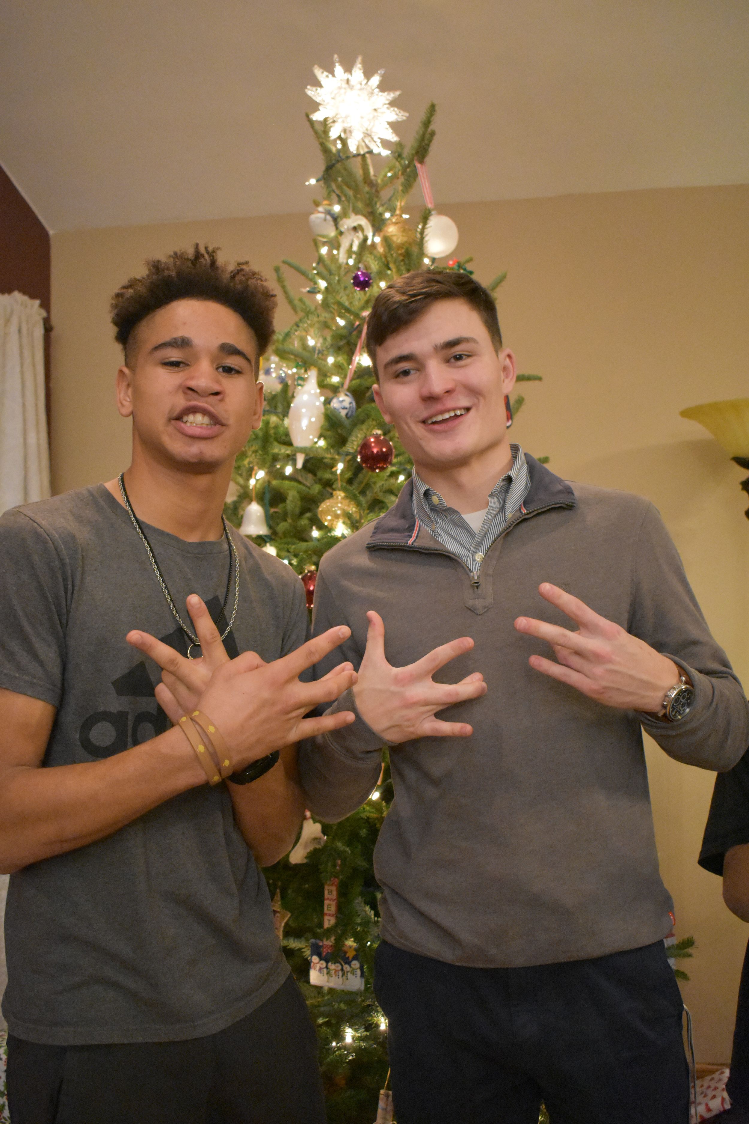 Two friends pose in front of a decorated Christmas tree making hand gestures.