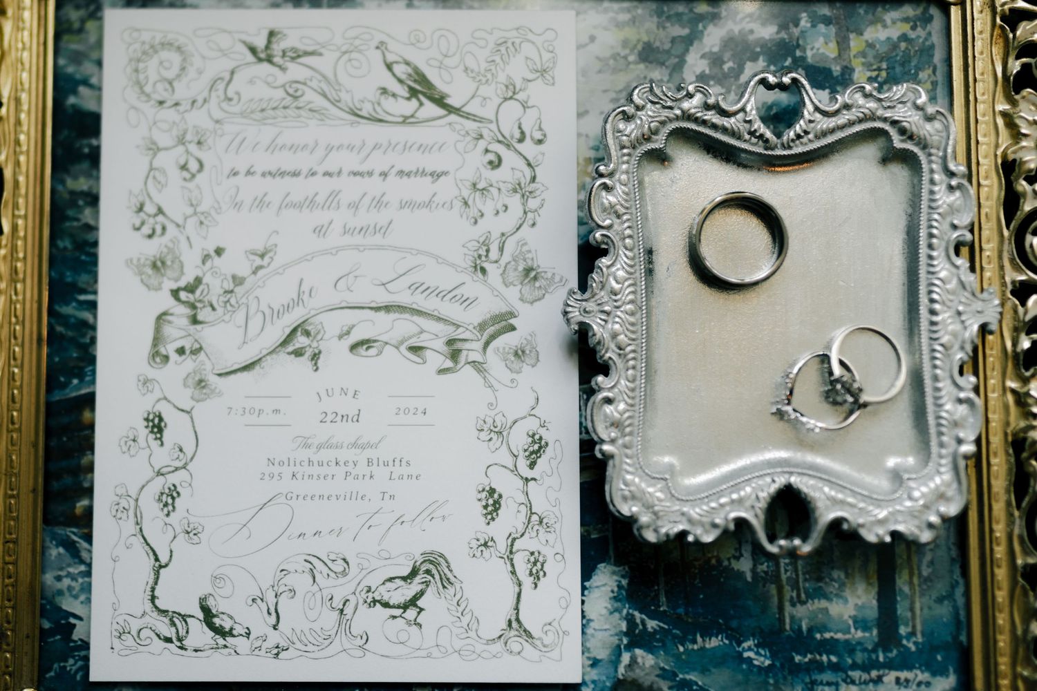 Vintage-style wedding invitations with ornate floral borders and calligraphy displayed in golden frames.