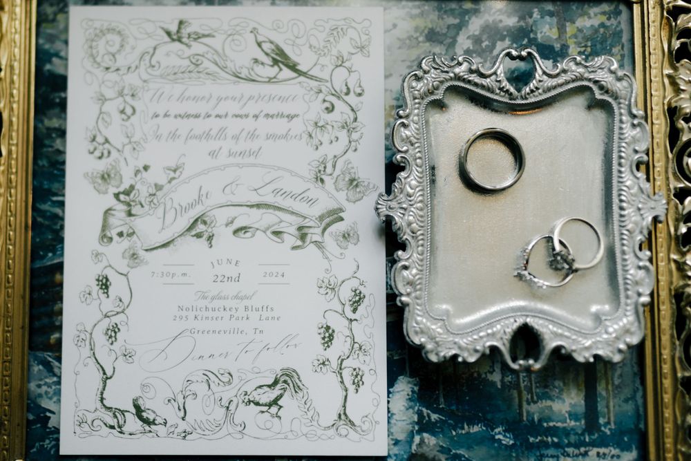 Vintage-style wedding invitations with ornate floral borders and calligraphy displayed in golden frames.