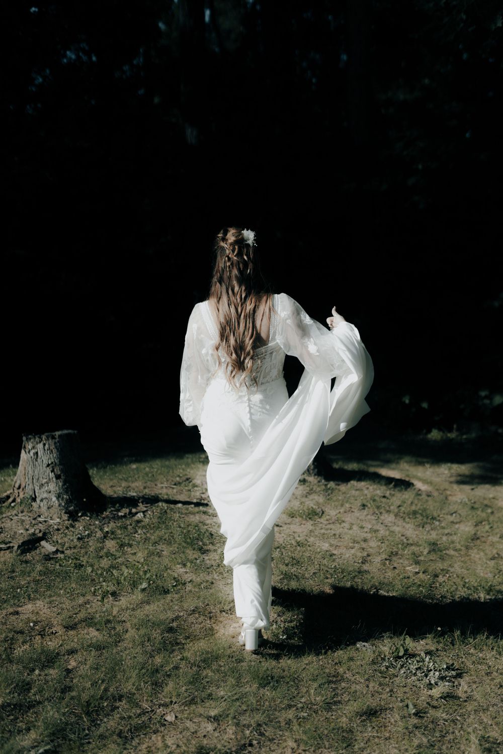 Ethereal scene of flowing white dress moving through a shadowy forest setting.