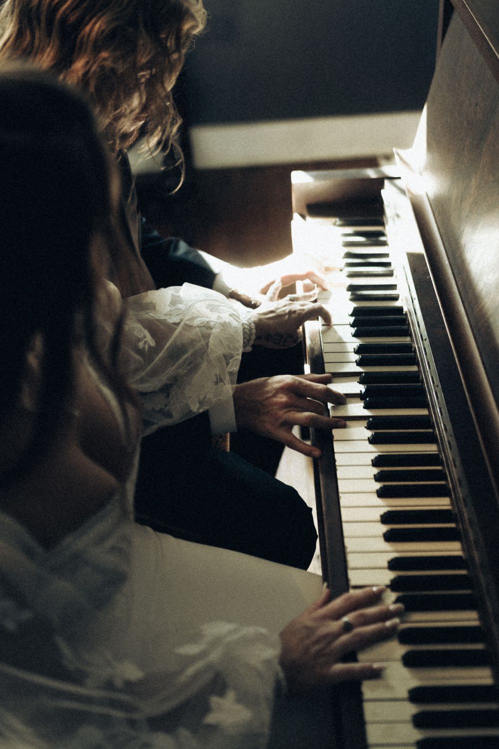 Hands playing piano keys in moody artistic lighting.