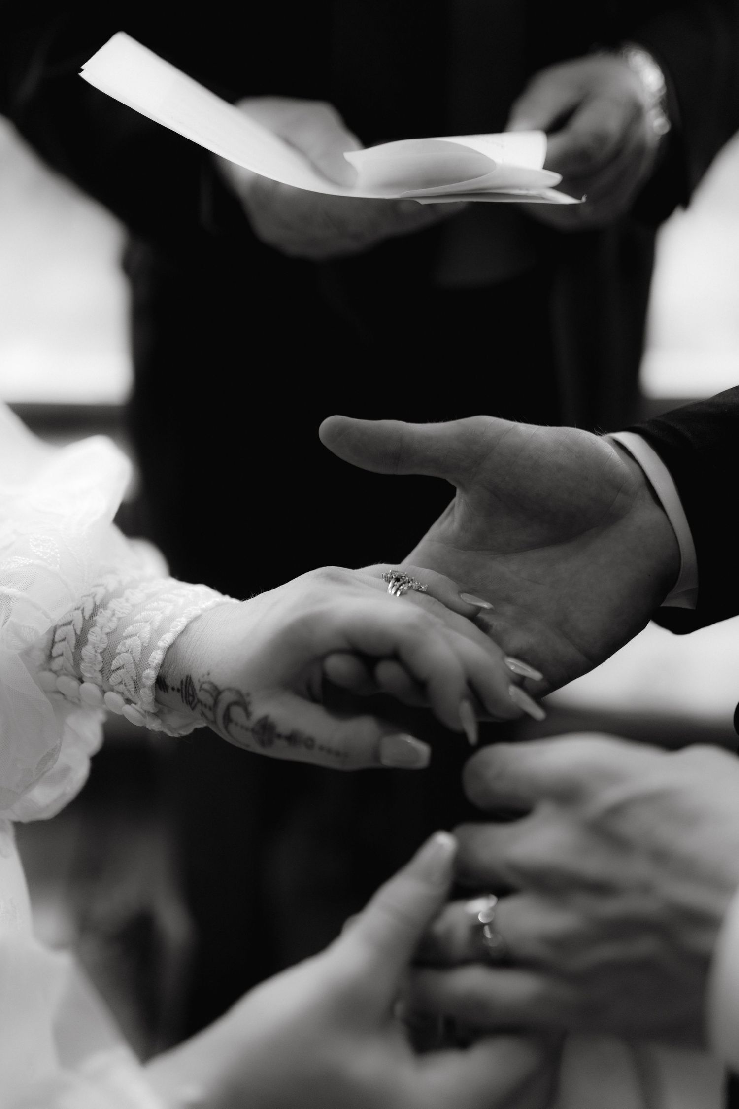 A close-up of hands during a wedding ceremony with rings and paper being exchanged.