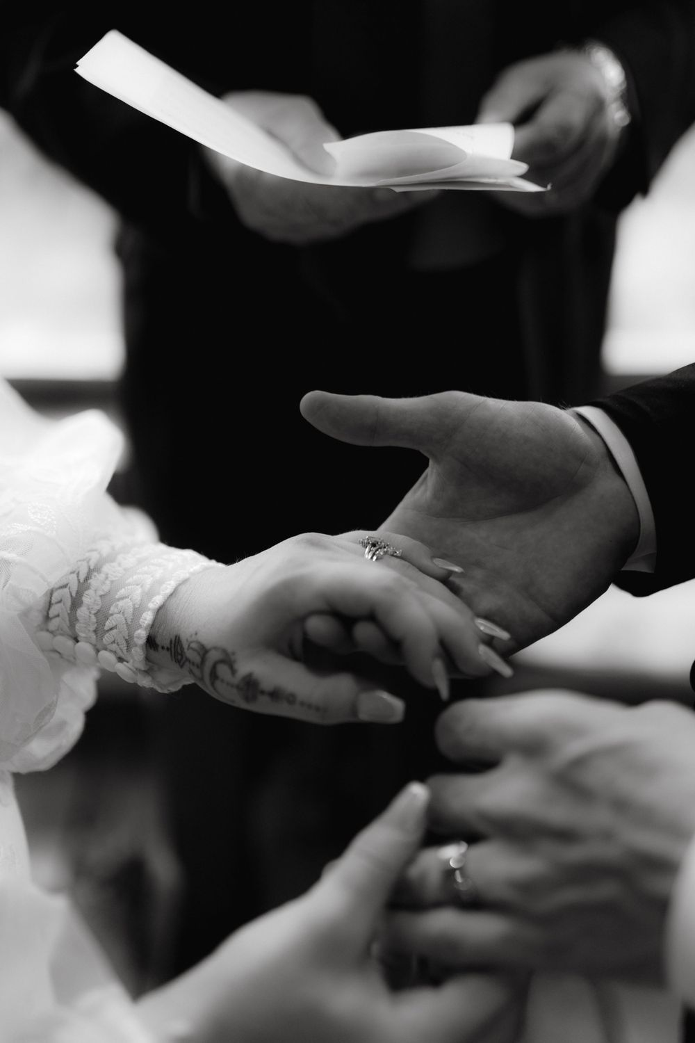 A close-up of hands during a wedding ceremony with rings and paper being exchanged.