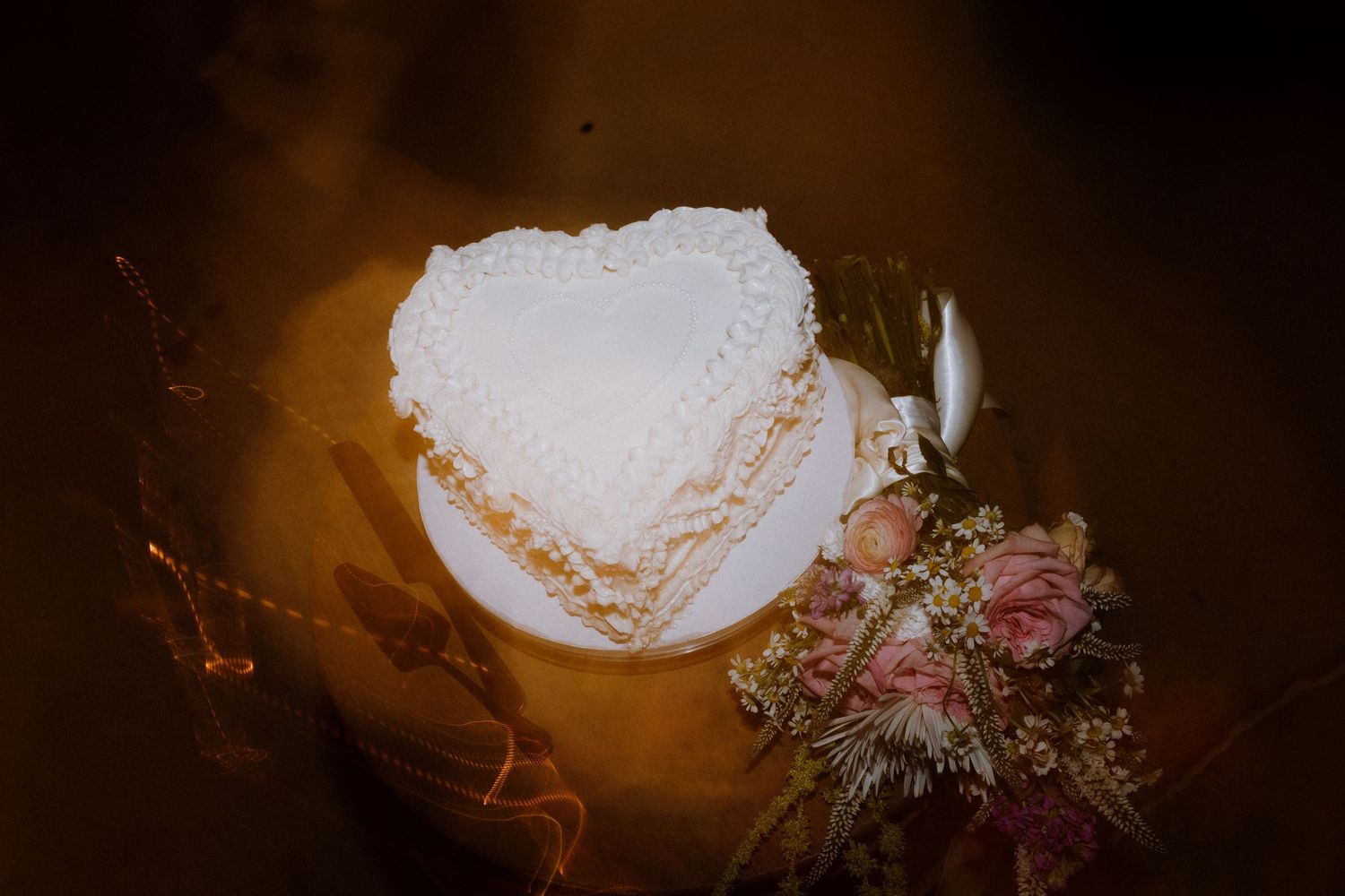 A heart-shaped wedding cake with soft lighting and pink floral decorations.