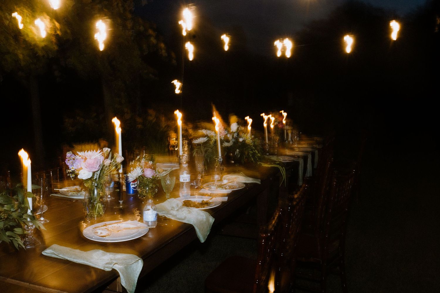 A romantic evening wedding reception table illuminated by hanging string lights.