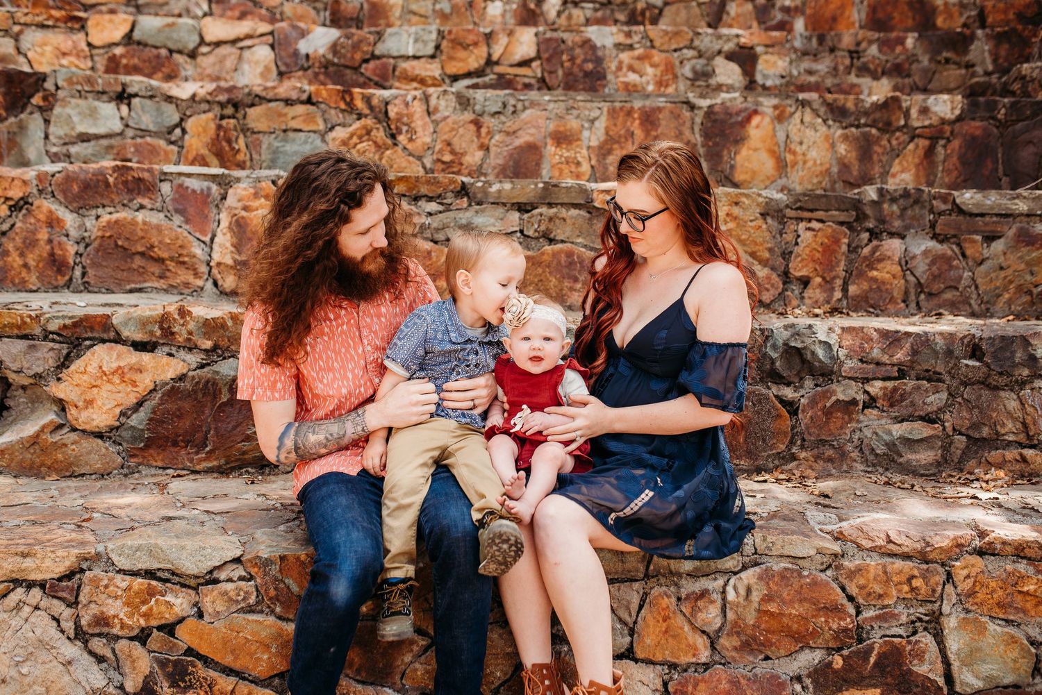 Three people sitting on stone steps sharing intimate moment together during outdoor portrait session.