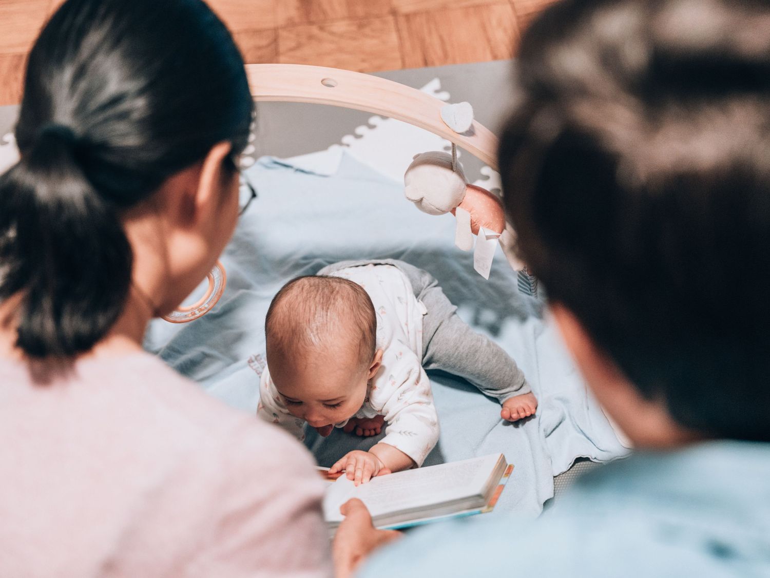 Baby lying on blanket during playtime with adults watching.