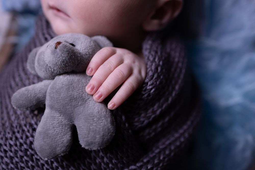 Close-up view of someone holding a soft gray plush toy against a dark textured background.