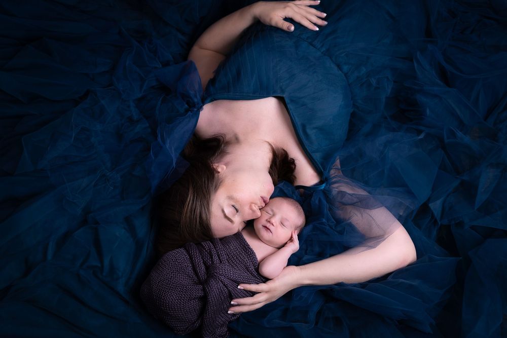 A sleeping infant rests peacefully on dark blue fabric while being gently cradled.