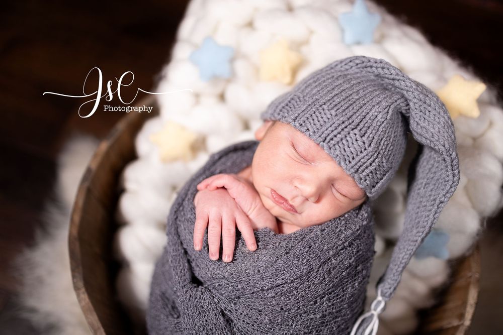Newborn photography with soft gray knit accessories and delicate lighting.