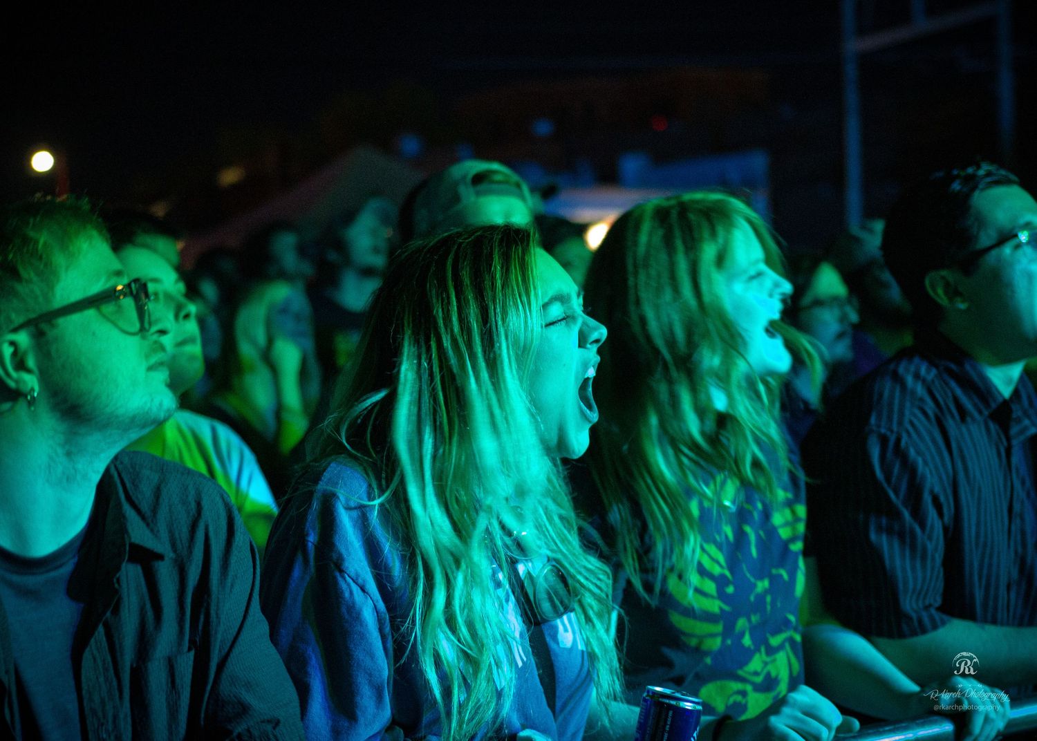 Concert audience watching performance with blue-green lighting in dark venue.