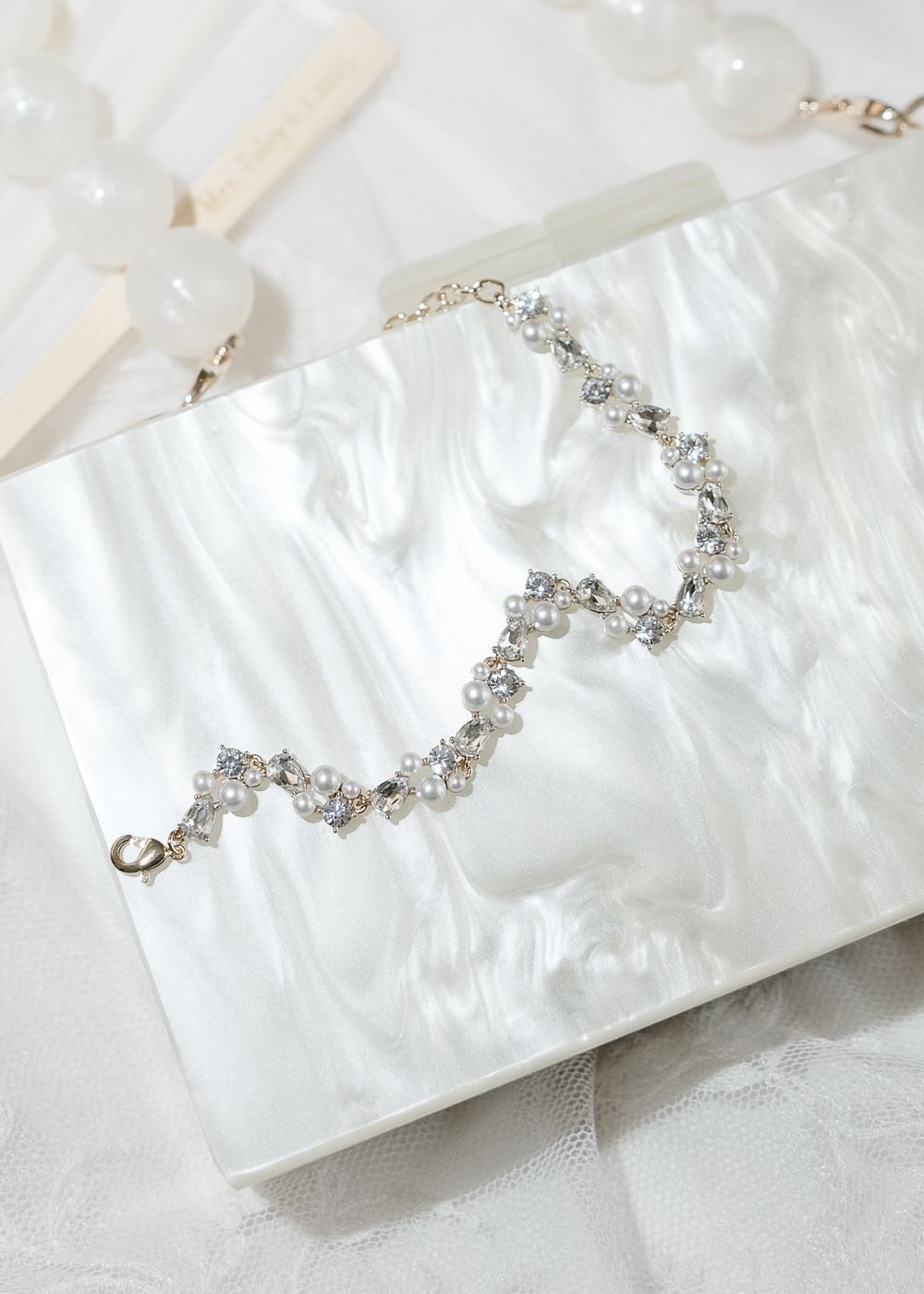 A string of delicate crystal beaded jewelry displayed against a pearlescent white surface.