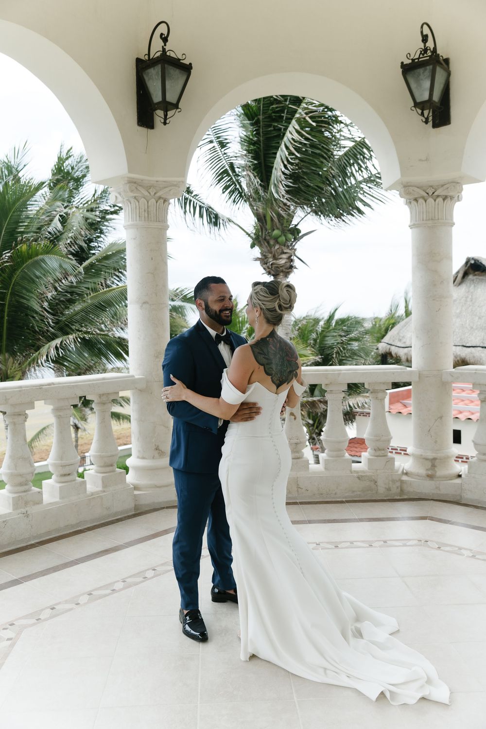 Wedding couple share romantic moments under white archways with palm trees swaying in tropical breeze at luxury venue.