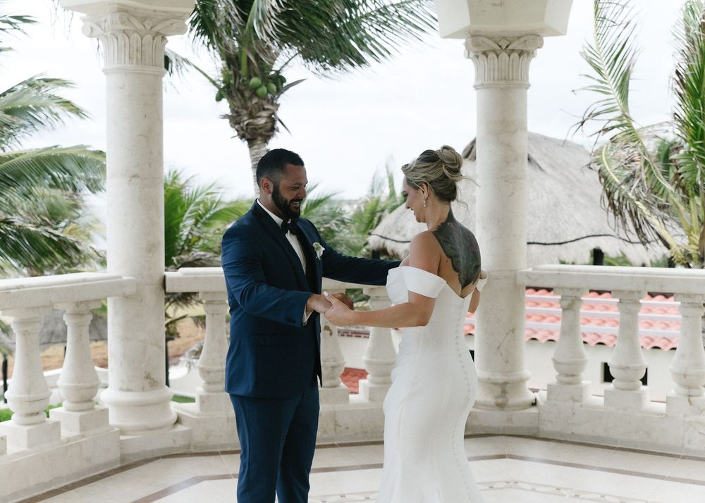 A romantic moment between newlyweds beneath white stone columns with swaying palm trees in the background.
