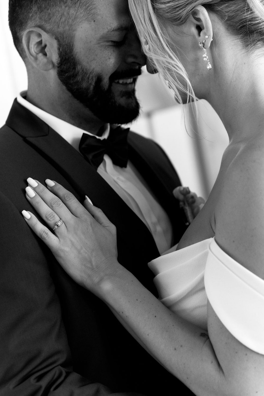 Close-up black and white wedding photo showing an intimate moment with bride's hand resting on groom's tuxedo.