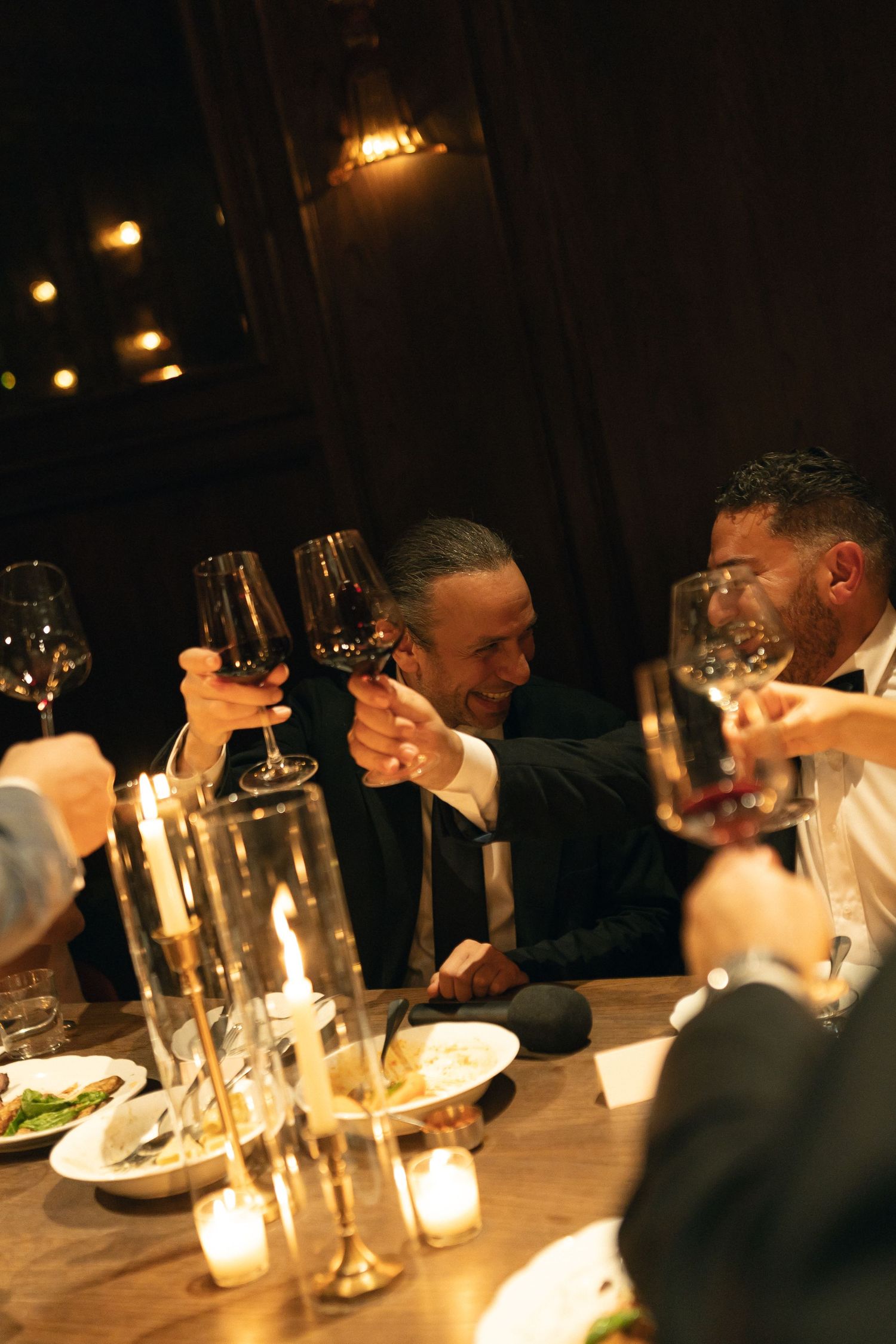 Friends enjoying drinks and conversation around a candlelit dinner table at a restaurant with wine glasses and plates. Documentary photos