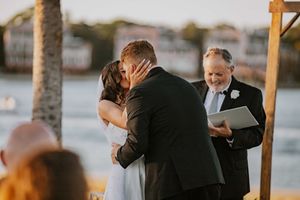 A couple shares an intimate moment during their wedding ceremony under a covered outdoor venue by the water.