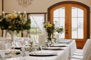 Elegant wedding reception table with white linens, yellow floral centerpieces, and fine place settings near French doors.