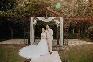 Bride and groom pose under a rustic wooden arch with white draping at an outdoor garden wedding ceremony.