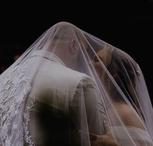 Bride and groom sharing a romantic kiss under a delicate lace wedding veil.