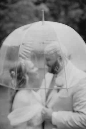 Black and white photo of a couple sharing a romantic kiss under a clear dome umbrella on their wedding day.