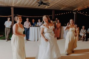 Bride dancing joyfully with bridesmaids in white gowns at outdoor wedding reception.
