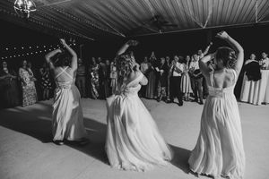 Bridesmaids and bride share joyful dance performance in black and white photo at wedding reception.