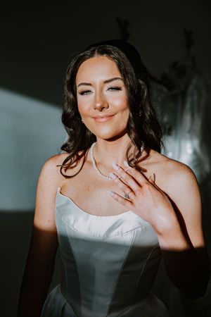 Bride in white strapless dress shows off wedding jewelry and makeup.