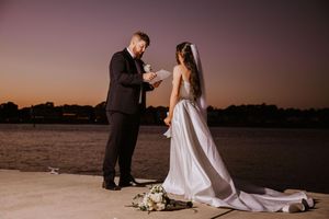 Couple poses for romantic sunset photos on a beach boardwalk with flowing wedding dress.