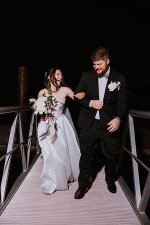 Playful wedding couple shares candid moments on a white wooden dock at night.