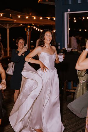 Wedding guests dancing and celebrating on wooden deck under string lights.