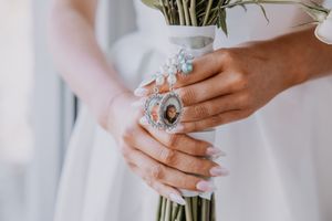 Close-up of hands holding a wedding bouquet with vintage jewelry and delicate manicure.