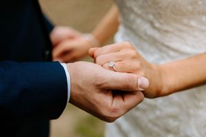 Groom placing a diamond engagement ring on bride's finger during wedding ceremony.