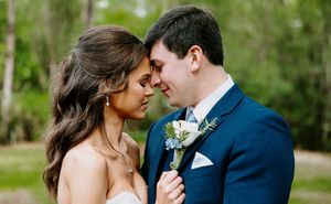 A bride and groom share an intimate forehead touch moment outdoors, wearing wedding attire with a floral boutonniere.