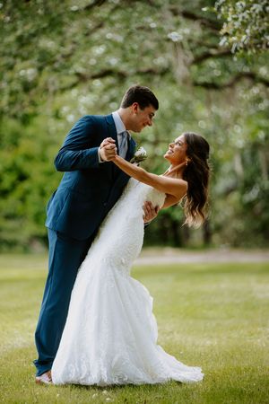 A bride and groom share a romantic dance outdoors, surrounded by lush green trees on their wedding day.