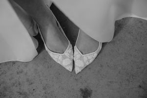 Close-up details of white bridal shoes on concrete floor.