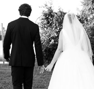Black and white photo of a bride and groom holding hands, walking away, bride wearing veil and white gown.