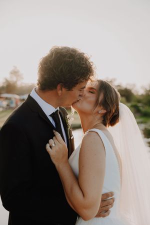 A bride and groom share a romantic kiss at golden hour, with the bride in a white gown and veil.
