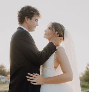A bride and groom share a romantic moment outdoors, with the groom tenderly holding the bride's face as she gazes up at him.