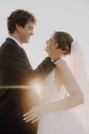 Joyful bride and groom sharing a tender moment with golden sunlight flare during outdoor wedding portrait.
