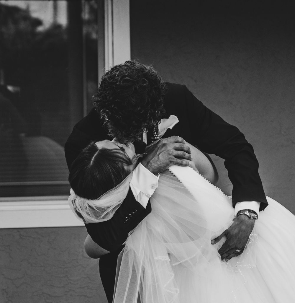 Black and white photo of a bride and groom sharing a romantic dip kiss on their wedding day.