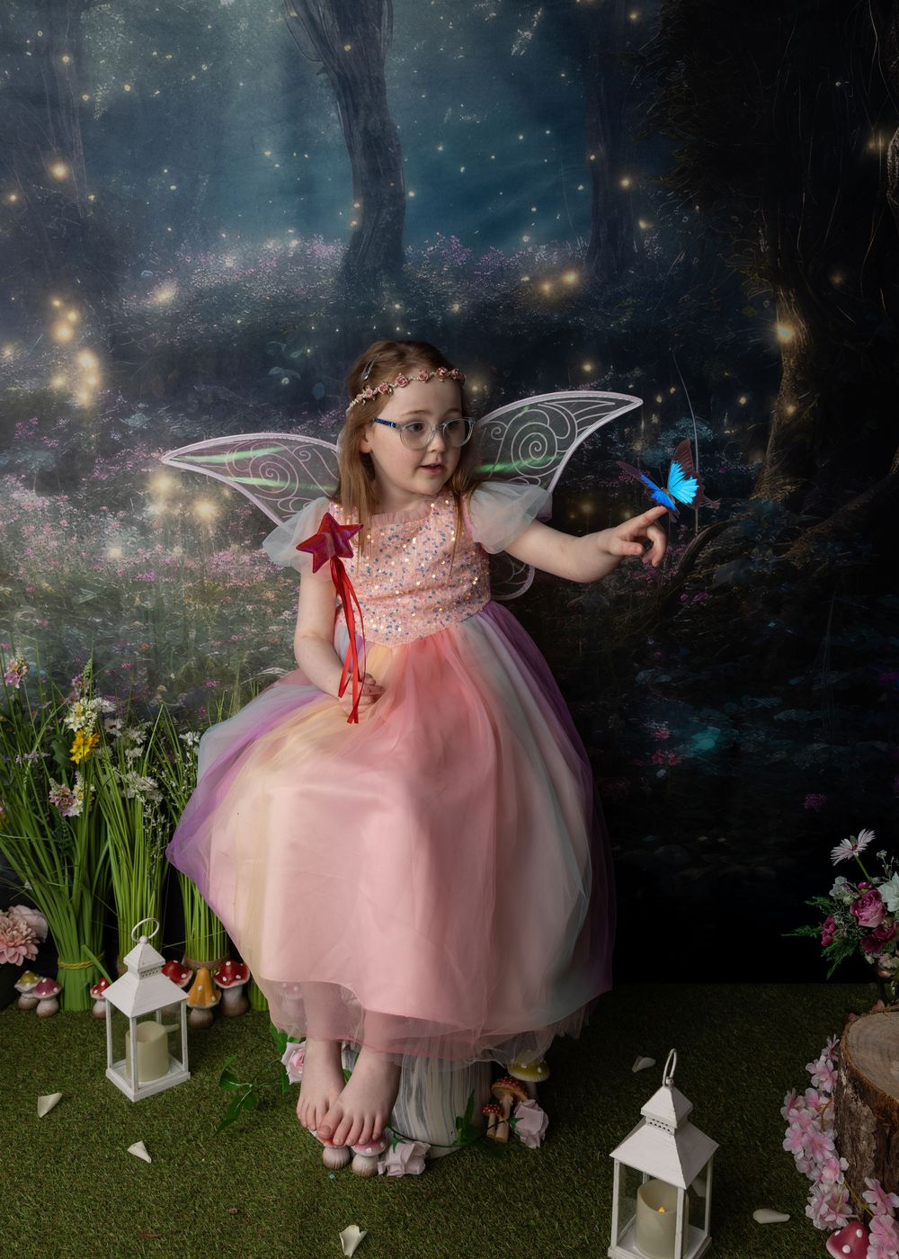 A magical fairy garden scene with twinkling lights, white lanterns, pink flowers and a butterfly in an enchanted forest setting.