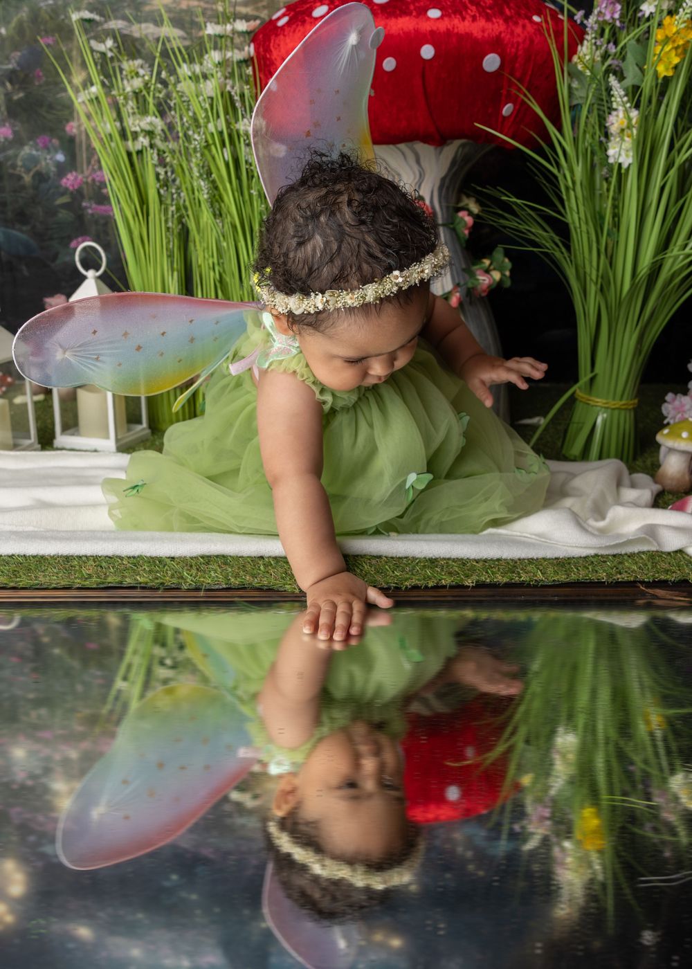 Reflection in a mirror shows a fairy-themed photo scene with wings, toadstool, and green dress against garden backdrop.